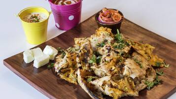 Una tabla de madera con pollo a la parrilla, una taza amarilla y una taza morada con salsa.