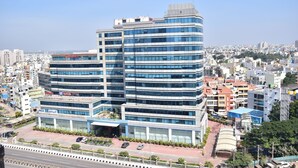 Um edifício comercial com várias andares e fachada de vidro moderna, rodeado por outros edifícios urbanos.