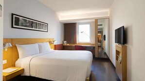 Quarto de hotel com uma cama grande, mesas de cabeceira, escrivaninha, televisão e janela.
