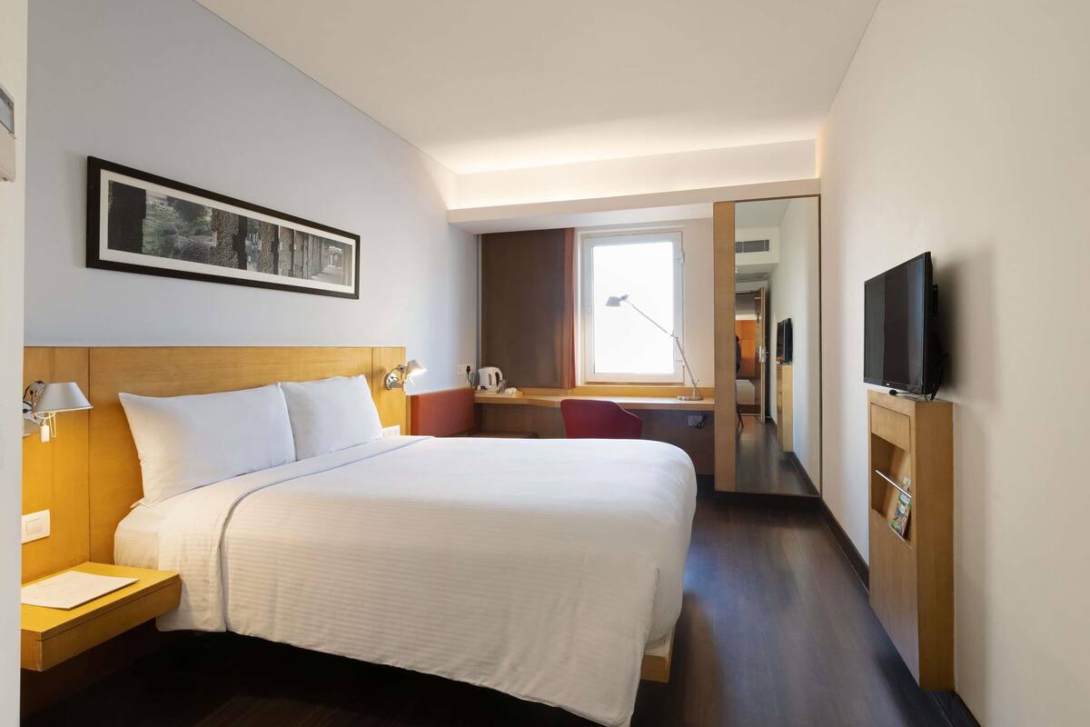 Ein Hotelzimmer mit einem großen Bett, Nachttischen, einem Schreibtisch, einem Fernseher und einem Fenster.