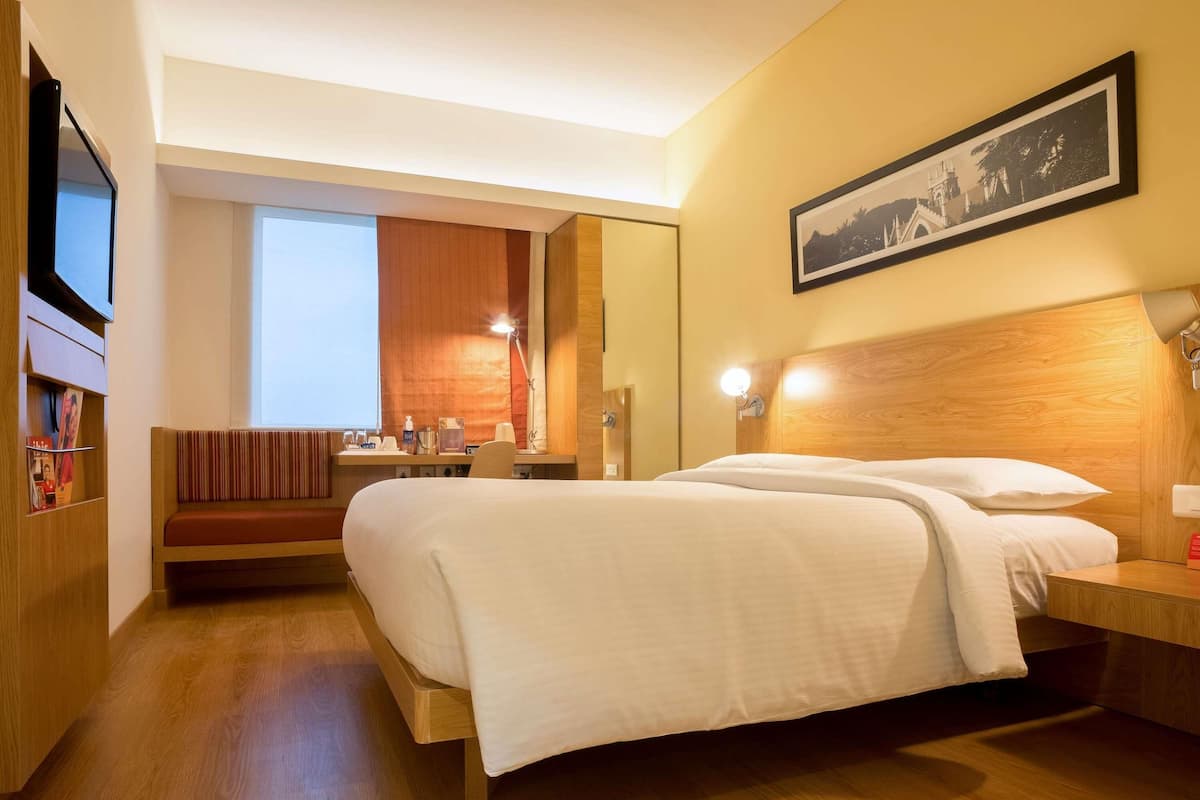 Ein Hotelzimmer mit einem großen Bett, einem Schreibtisch, einem Sessel, einem Fernseher und einem gerahmten Bild an der Wand.