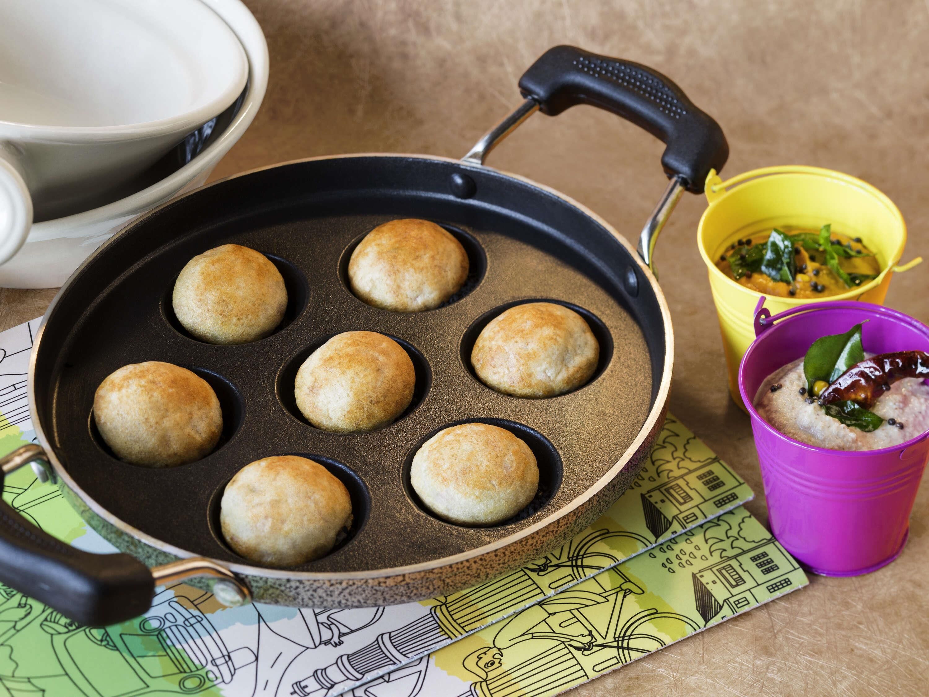 A pan with six round items, a yellow cup with food, and a purple cup with a beverage.