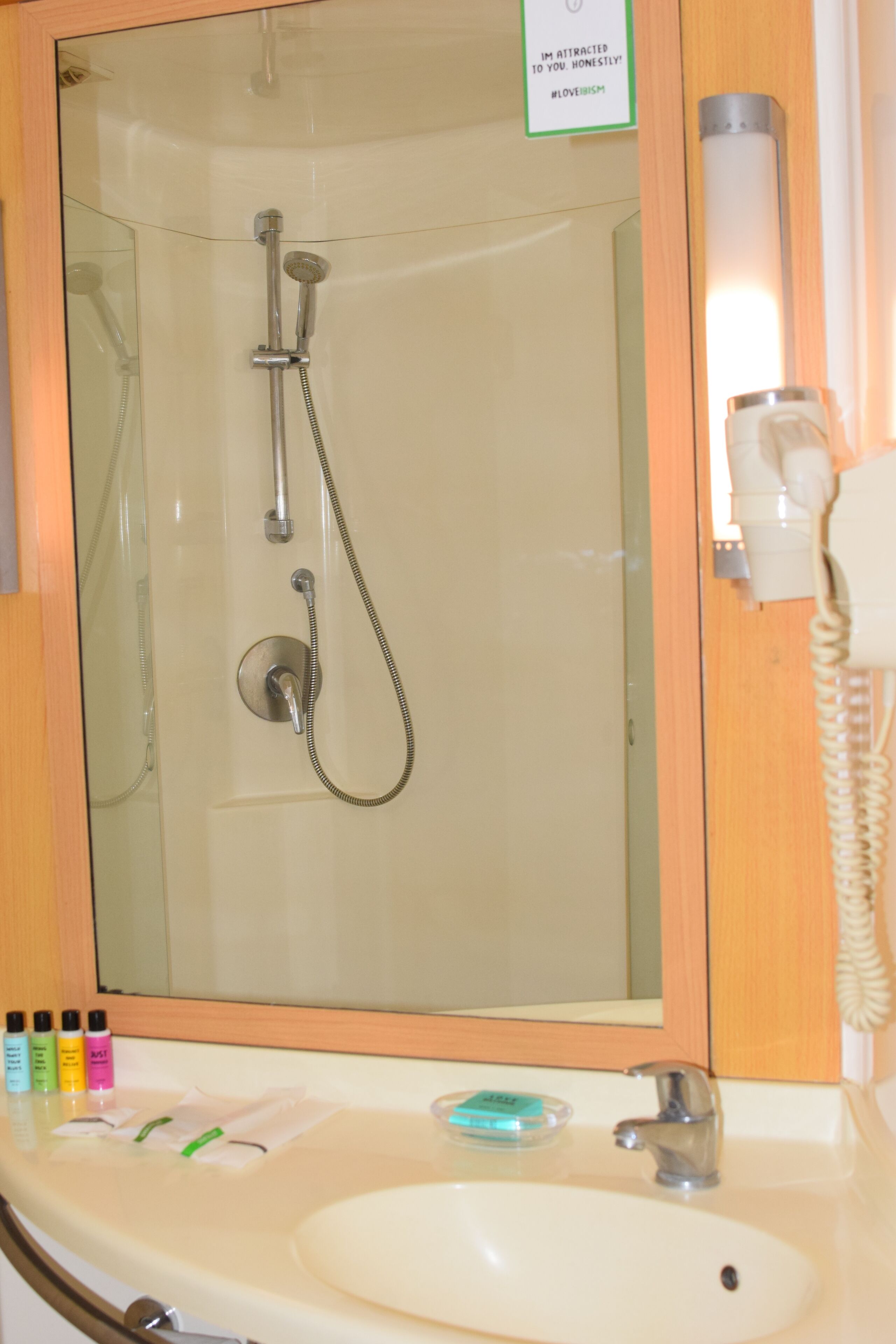 A bathroom with a glass-enclosed shower, a sink with toiletries, and a telephone.