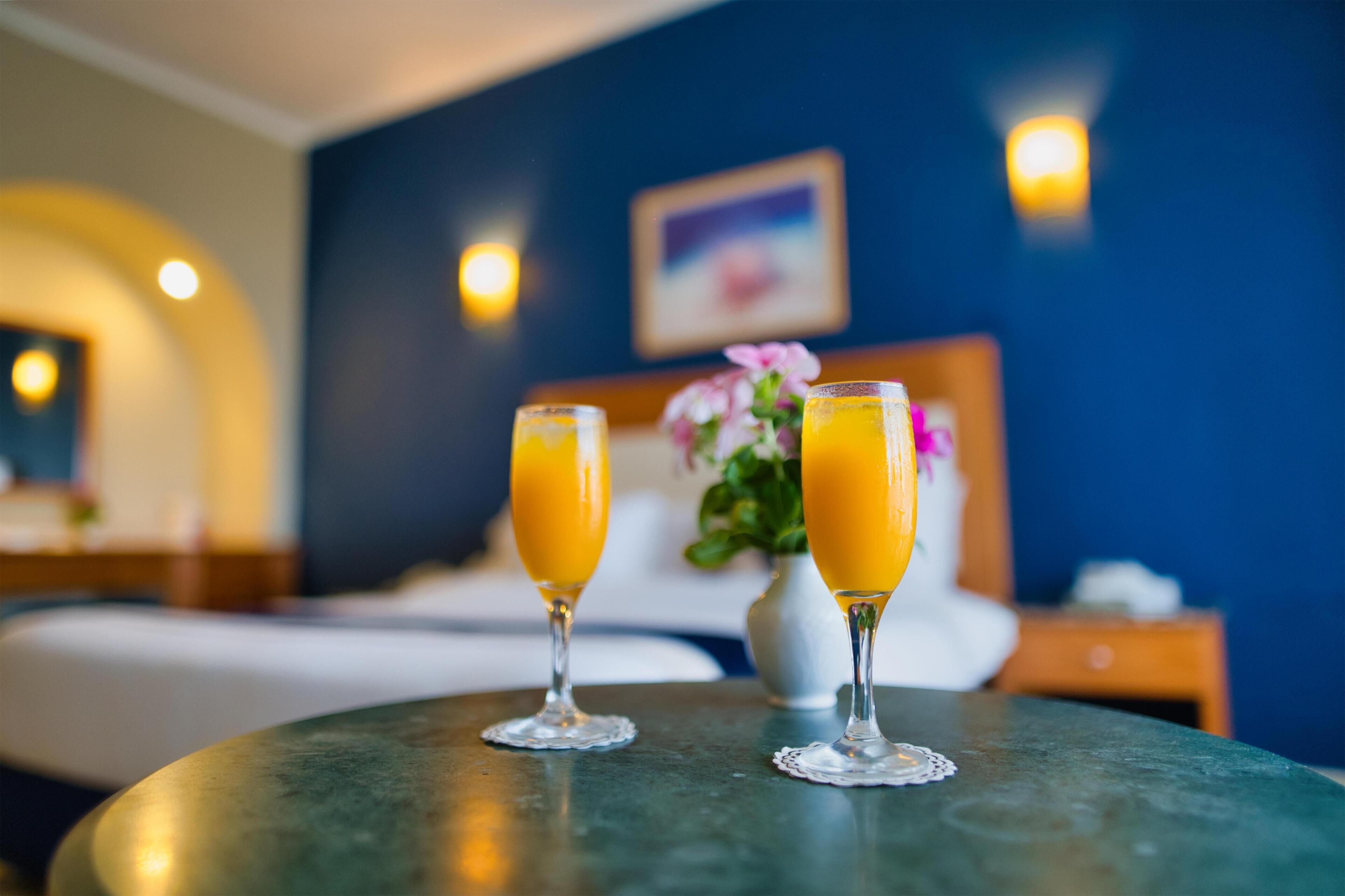 A hotel room with a bed, a nightstand, and two glasses of orange juice on a table.