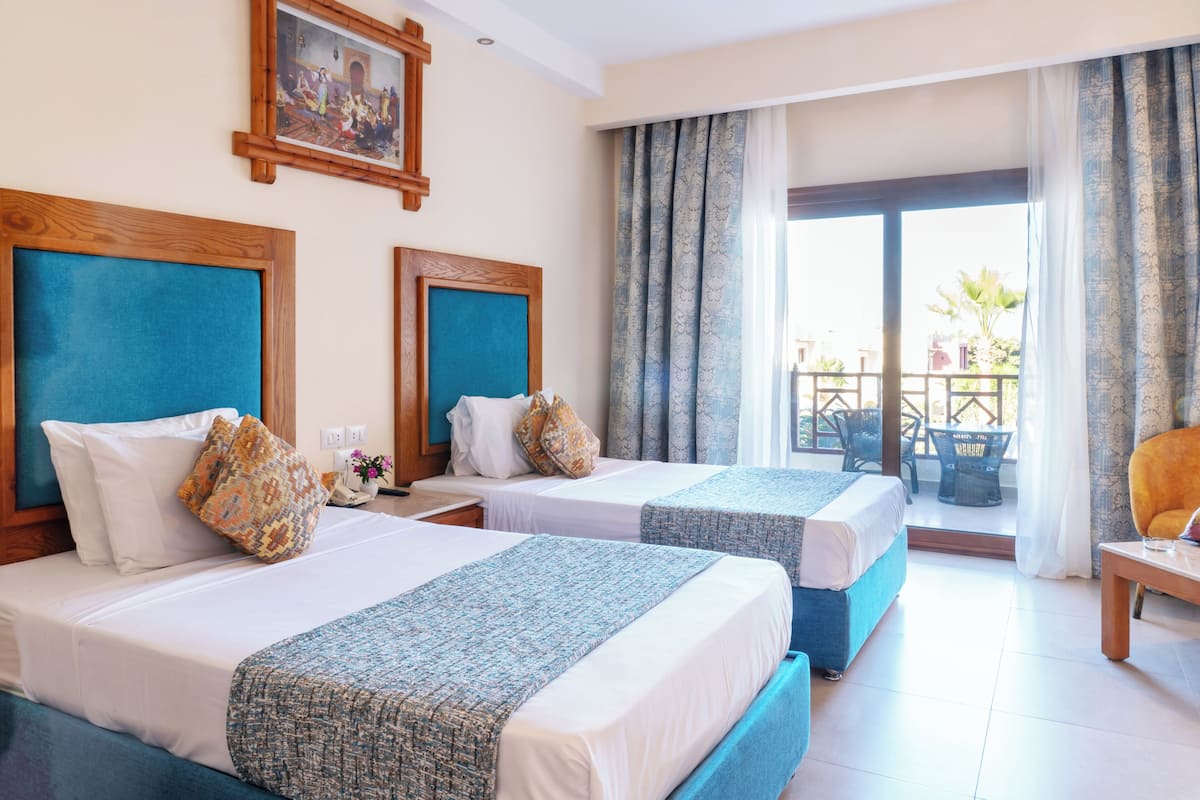 Habitación de hotel con dos camas, un balcón y vistas al exterior.