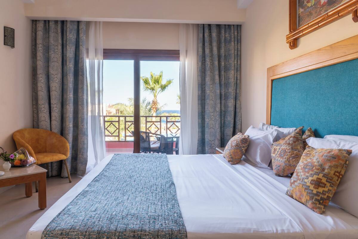 Habitación de hotel con cama, una silla, una mesa y un balcón con vistas.