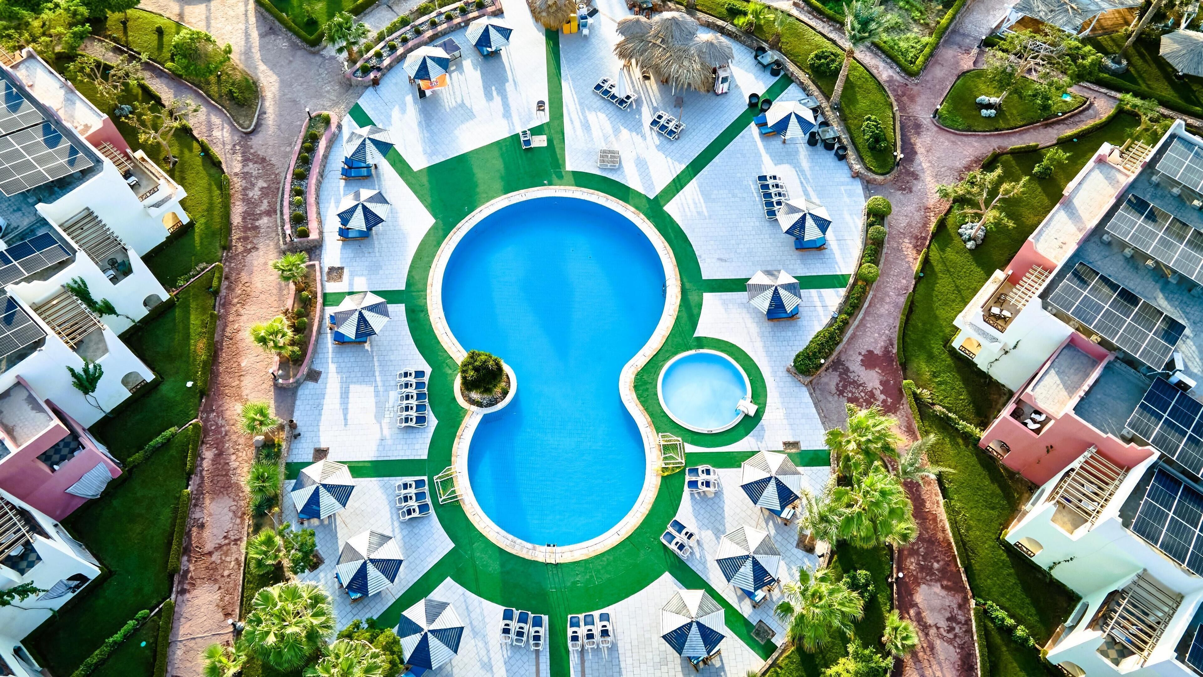 An aerial view of a resort with a central swimming pool, sun loungers, and umbrellas.
