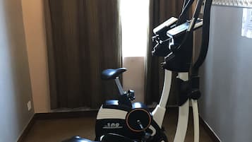 An exercise bike in a hotel room with a carpeted floor and a window with curtains.
