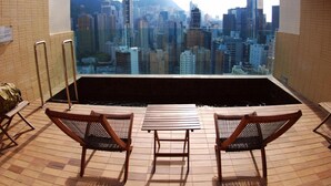 Une terrasse sur le toit offrant une vue sur les gratte-ciel de la ville, une petite piscine et deux chaises en bois.