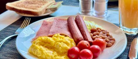 Un plato de desayuno con huevos, jamón, salchichas, tomates y frijoles.