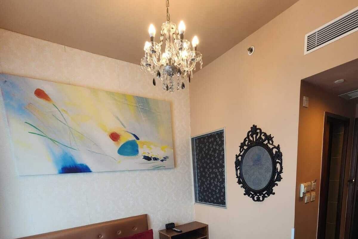 Une chambre d’hôtel avec un grand lit, un lustre, un tableau, un miroir et une porte.