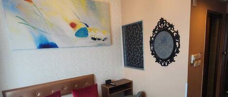 A hotel room with a large bed, a chandelier, a painting, a mirror, and a door.
