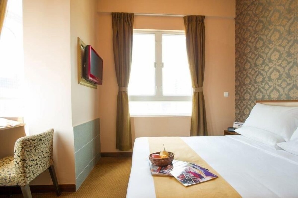 A hotel room with a bed, a chair, a television, and a window with curtains.