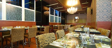 Un restaurante con sillas y mesas estampadas, ventanas amplias y candelabros.