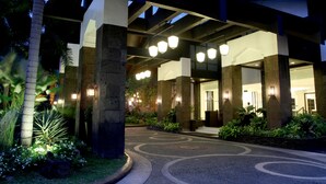 A hotel entrance with a curved pathway, palm trees, and a well-lit reception area. - Sulo Riviera Hotel (Quezon City)