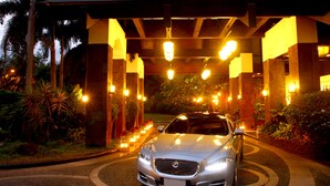 A silver car parked under a covered entrance with a series of lights and a well-maintained garden. - Sulo Riviera Hotel (Quezon City)