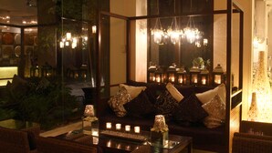 A cozy seating area with a cushioned sofa, a glass coffee table, and a decorative mirror reflecting a chandelier and interior lights. - Sulo Riviera Hotel (Quezon City)