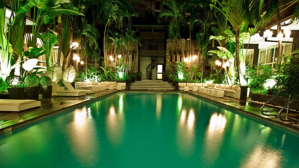 A pool area with a central staircase, surrounded by lush greenery and ambient lighting. - Sulo Riviera Hotel (Quezon City)