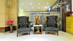 Un espace d’accueil comprenant deux fauteuils en cuir noir, une statue représentant un homme jouant de la contrebasse et un vase orné de fleurs roses.
