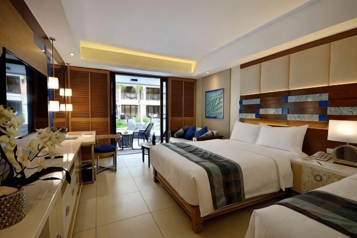 A hotel room with two beds, a desk, and a view of the outdoors.