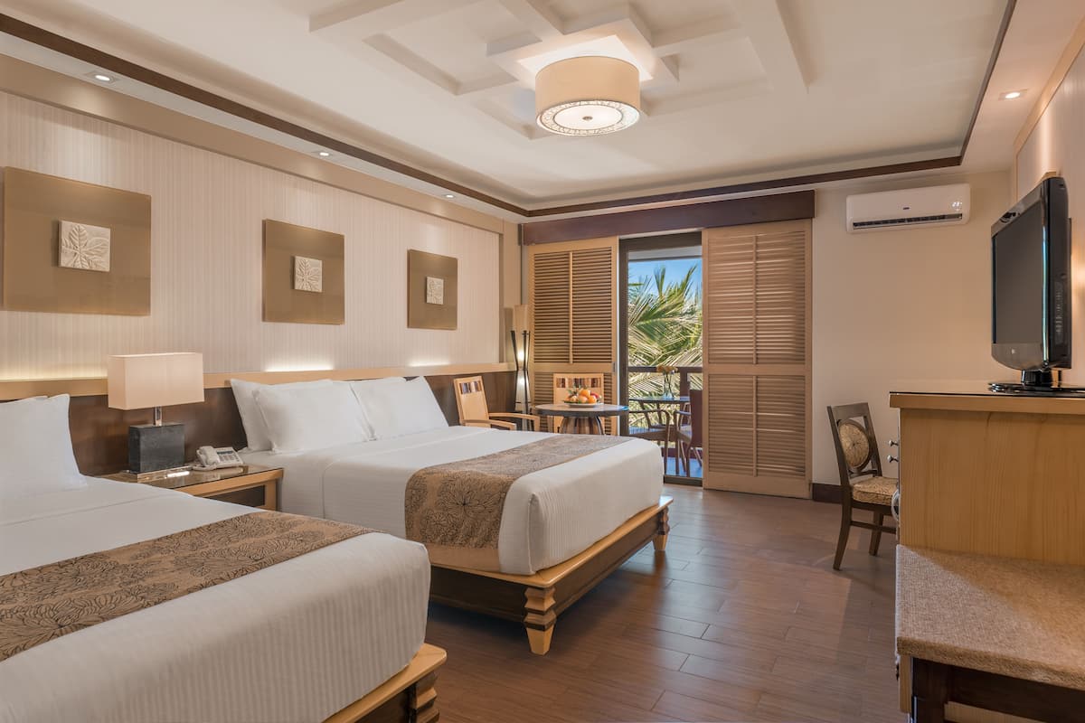 A hotel room with two beds, a desk, a chair, a television, and a balcony with a view of palm trees.