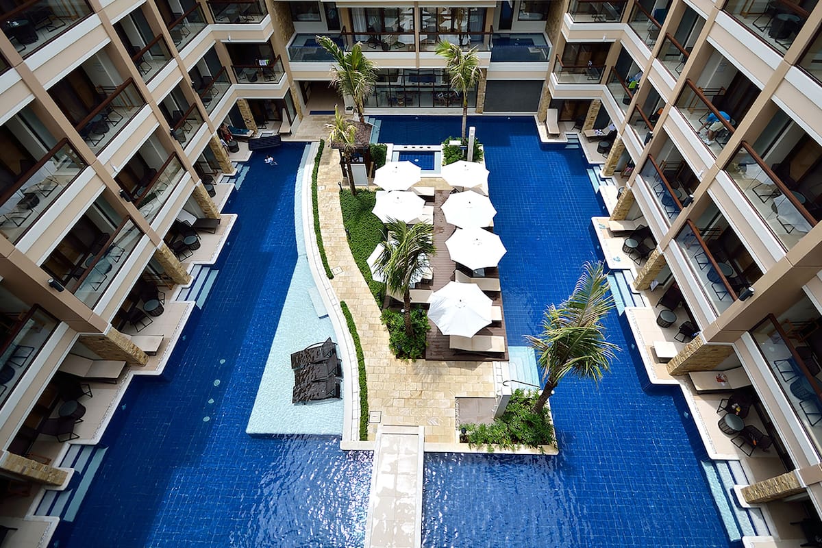 A multi-level hotel with a central swimming pool, outdoor seating areas, and balconies.