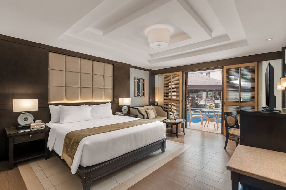 A modern hotel room with a large bed, bedside tables, a desk, and a view of the pool area.