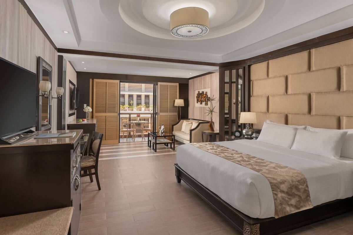 A hotel room with a large bed, a desk with a TV, a sofa, and a balcony with a view.