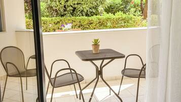 Un balcón con una mesa, dos sillas, una planta en maceta y vistas al follaje y árboles.
