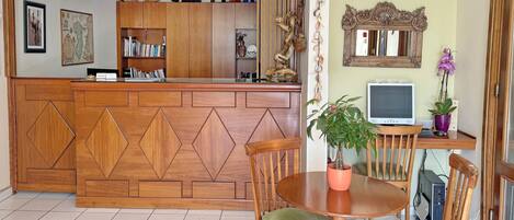 A reception area with a wooden counter, bookshelves, a television, and a potted plant.