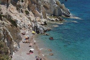 A rocky beach with clear water, umbrellas, and people. - Emporios Bay Hotel (Chios)