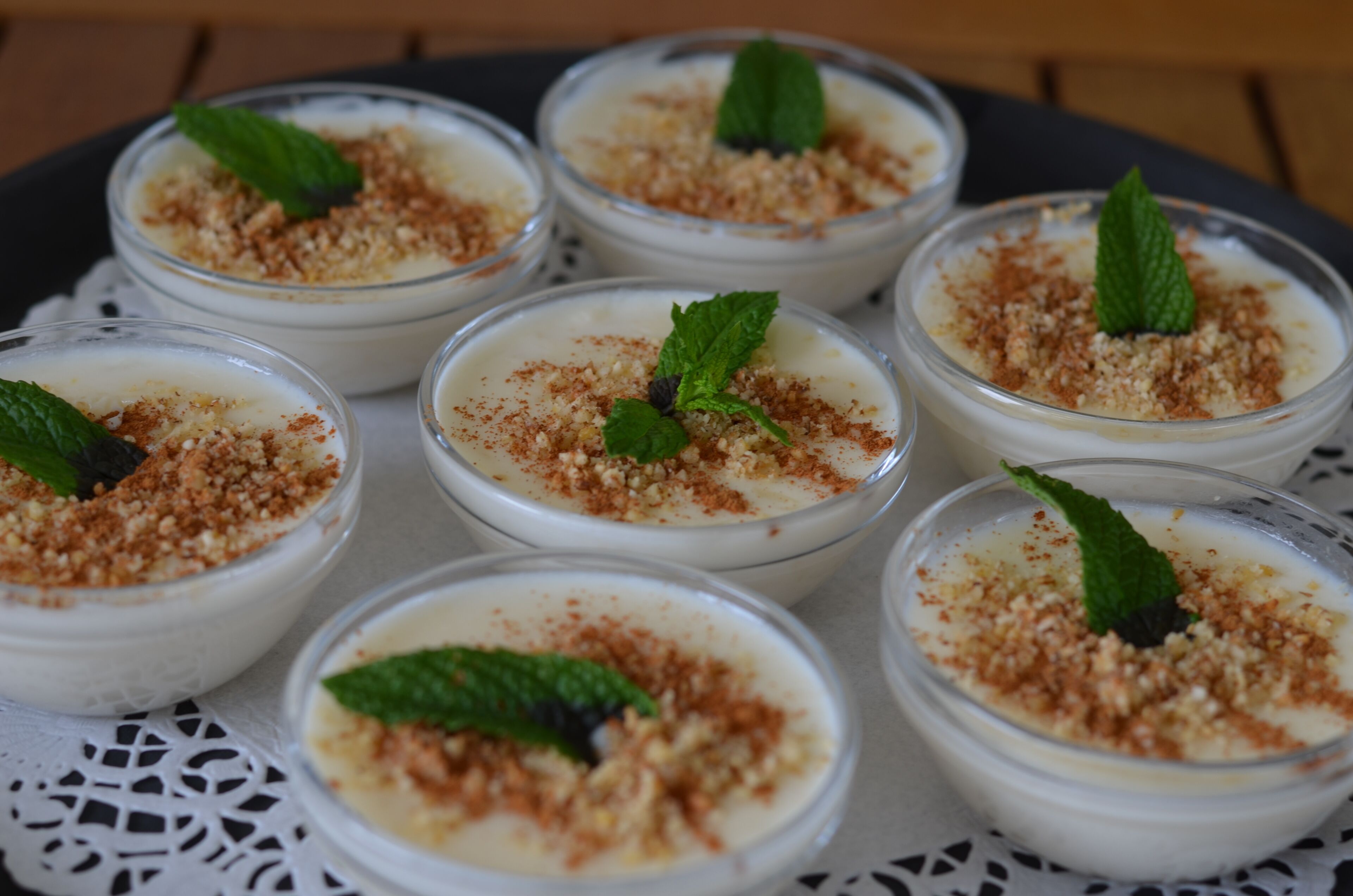 Six glass bowls of dessert with a crumbly topping and mint leaves.