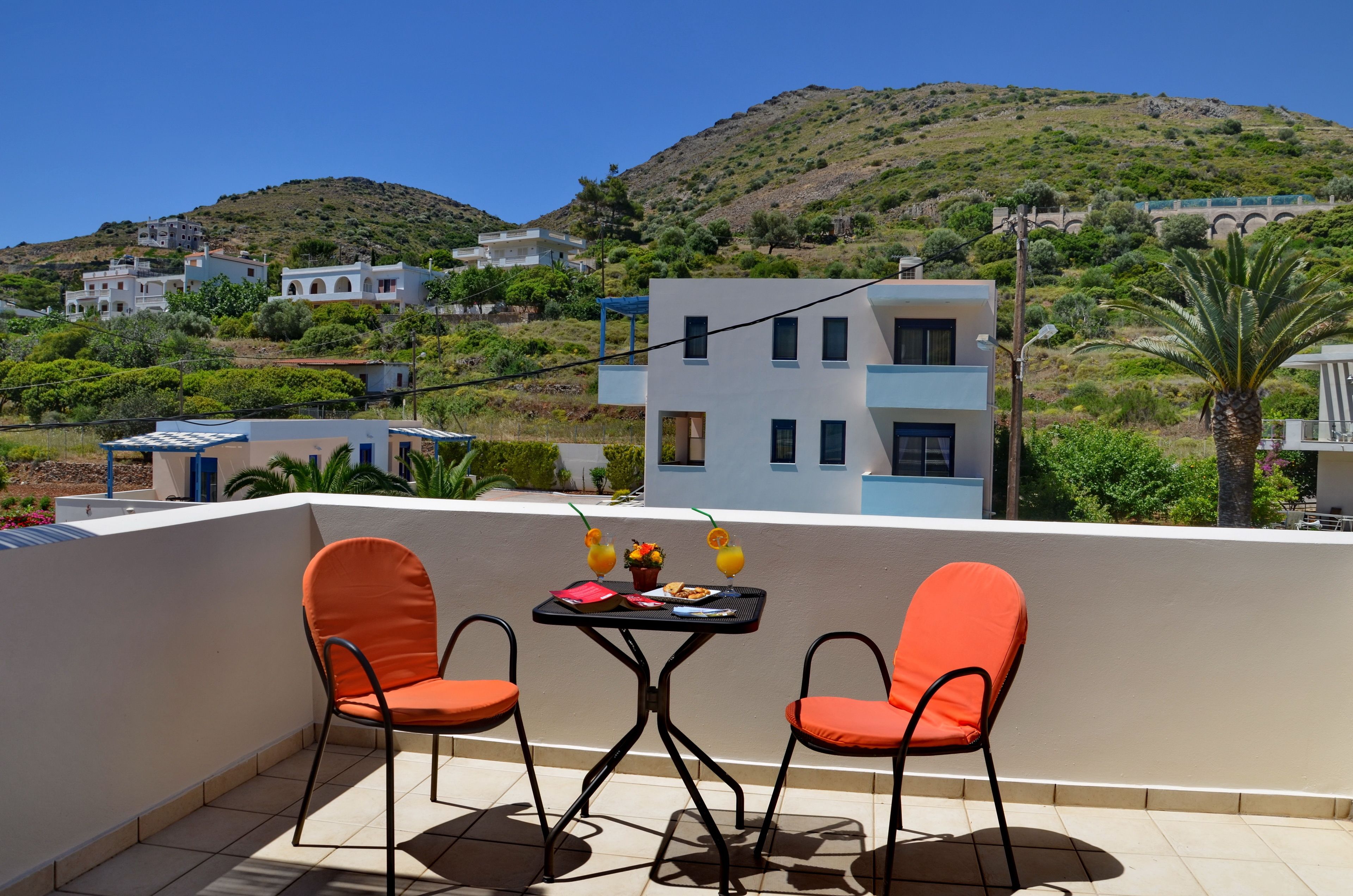 A terrace with two orange chairs and a table, overlooking a hillside with buildings.