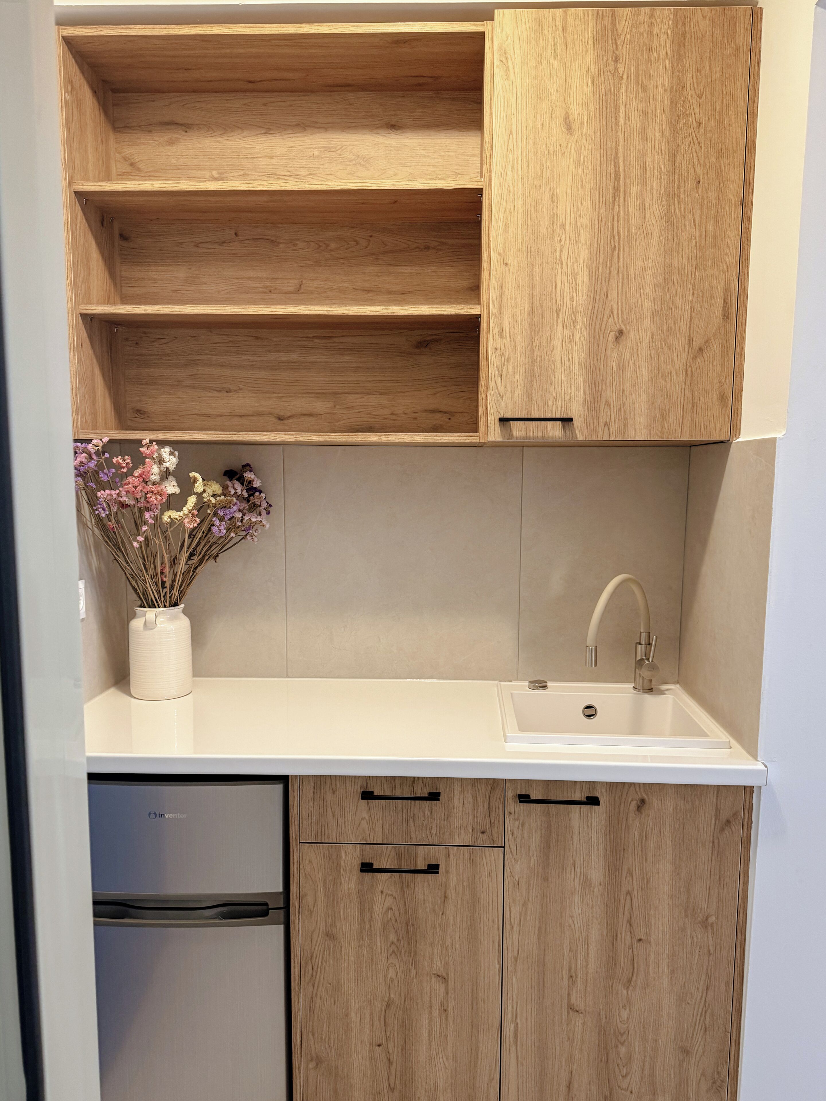 A kitchen with wooden cabinets, a white countertop, a sink, and a vase with dried flowers.