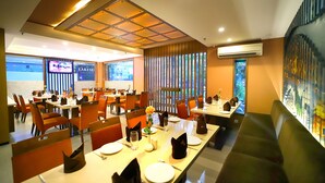 A restaurant with multiple tables, chairs, and a large window with a view. - Southern Plaza (Kolkata)
