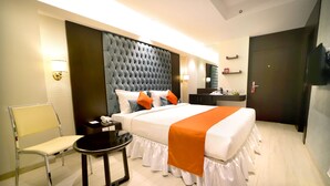 A hotel room with a large bed, a bedside table, a chair, and a small table. - Southern Plaza (Kolkata)