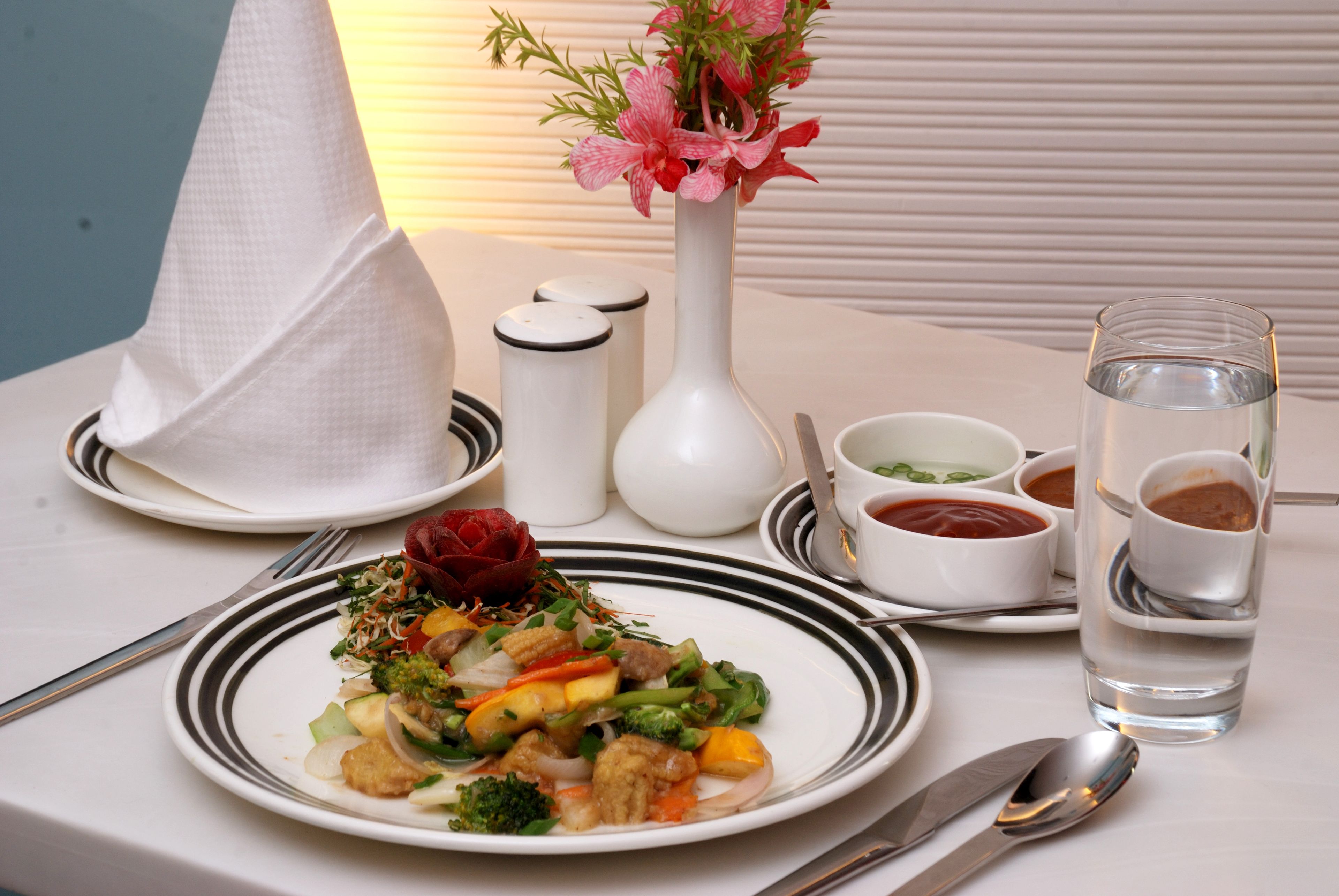 A dining table with a plate of food, a vase with flowers, condiments, and a glass of water.