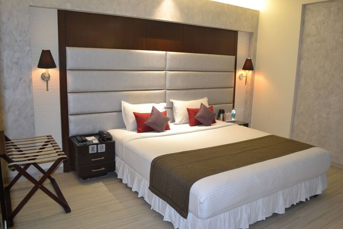 A hotel room with a large bed, bedside lamps, a nightstand, a chair, and a wooden floor.