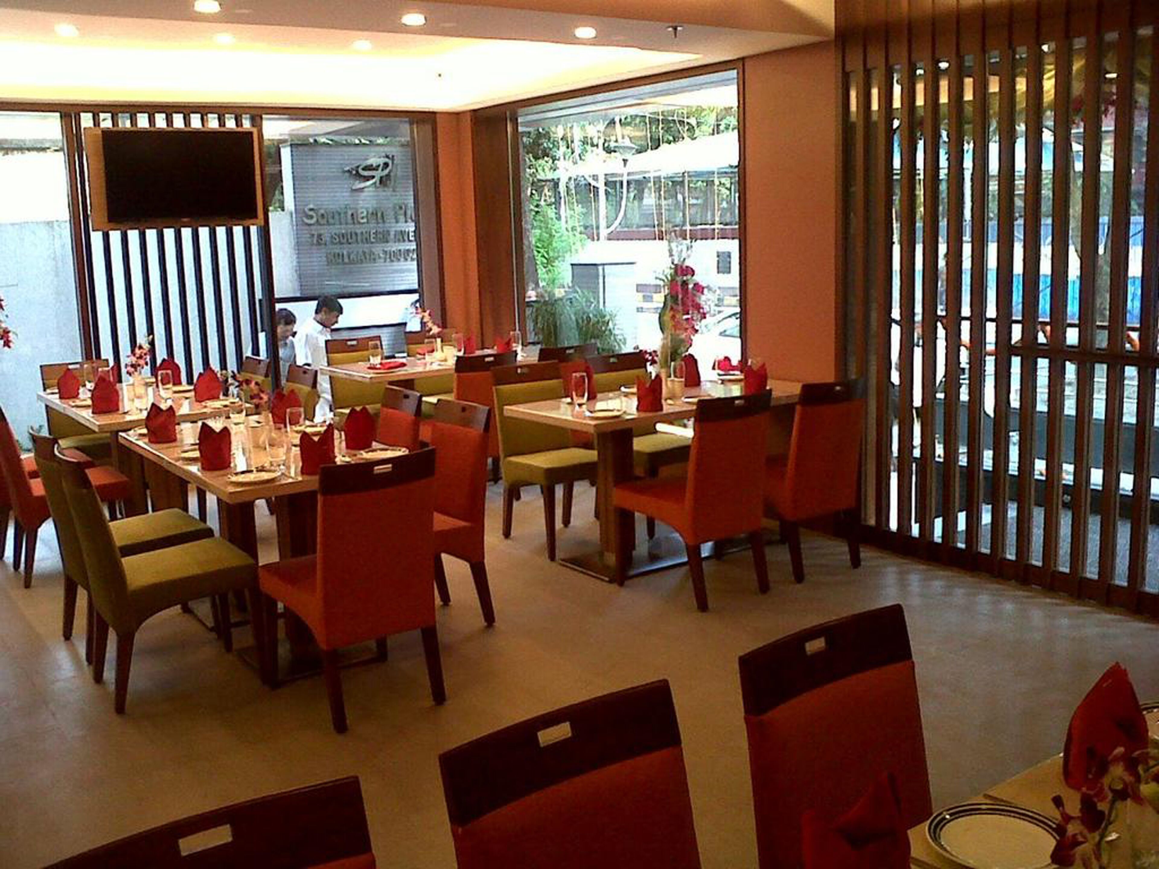 A restaurant with multiple tables and chairs, a TV screen on the wall, and a view of the outside through large windows.
