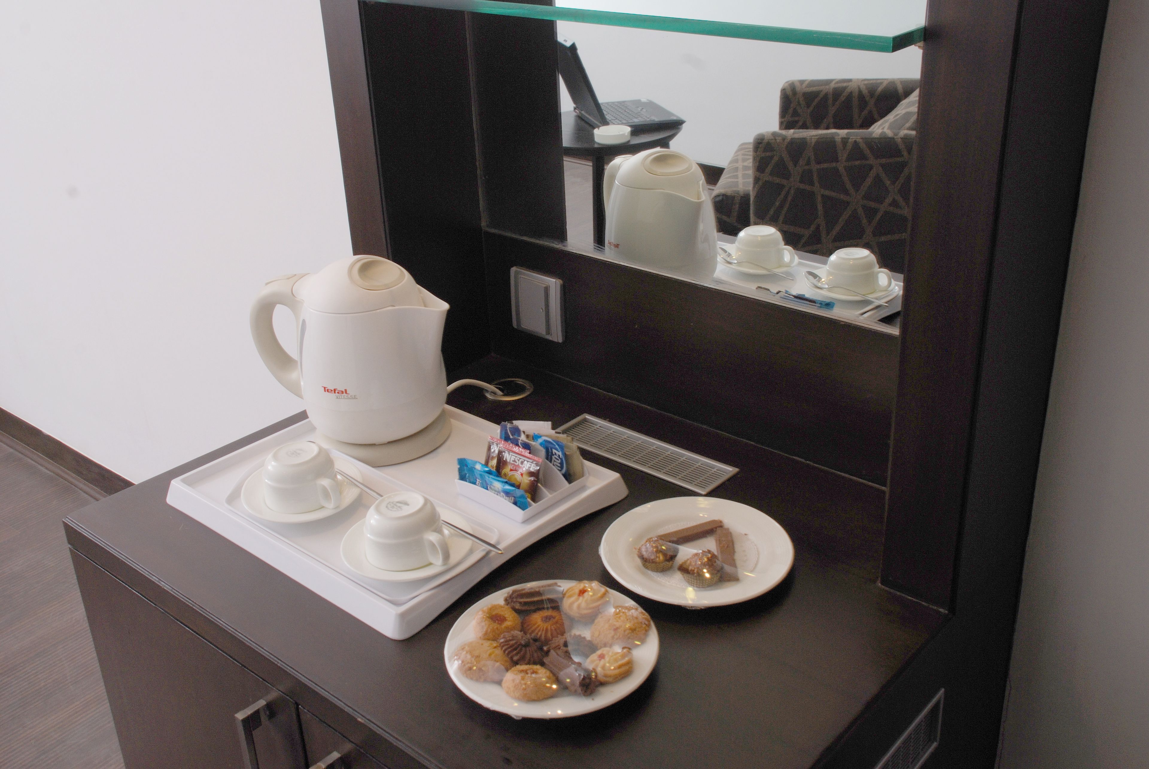 Une chambre d’hôtel équipée d’un coin café, d’un ordinateur portable posé sur une petite table et d’un lit recouvert d’une couverture à motifs.