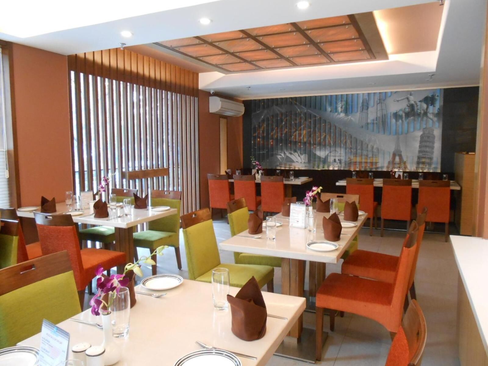 Un restaurante con varias mesas y sillas, un techo con iluminación empotrada y un mural en la pared de fondo.