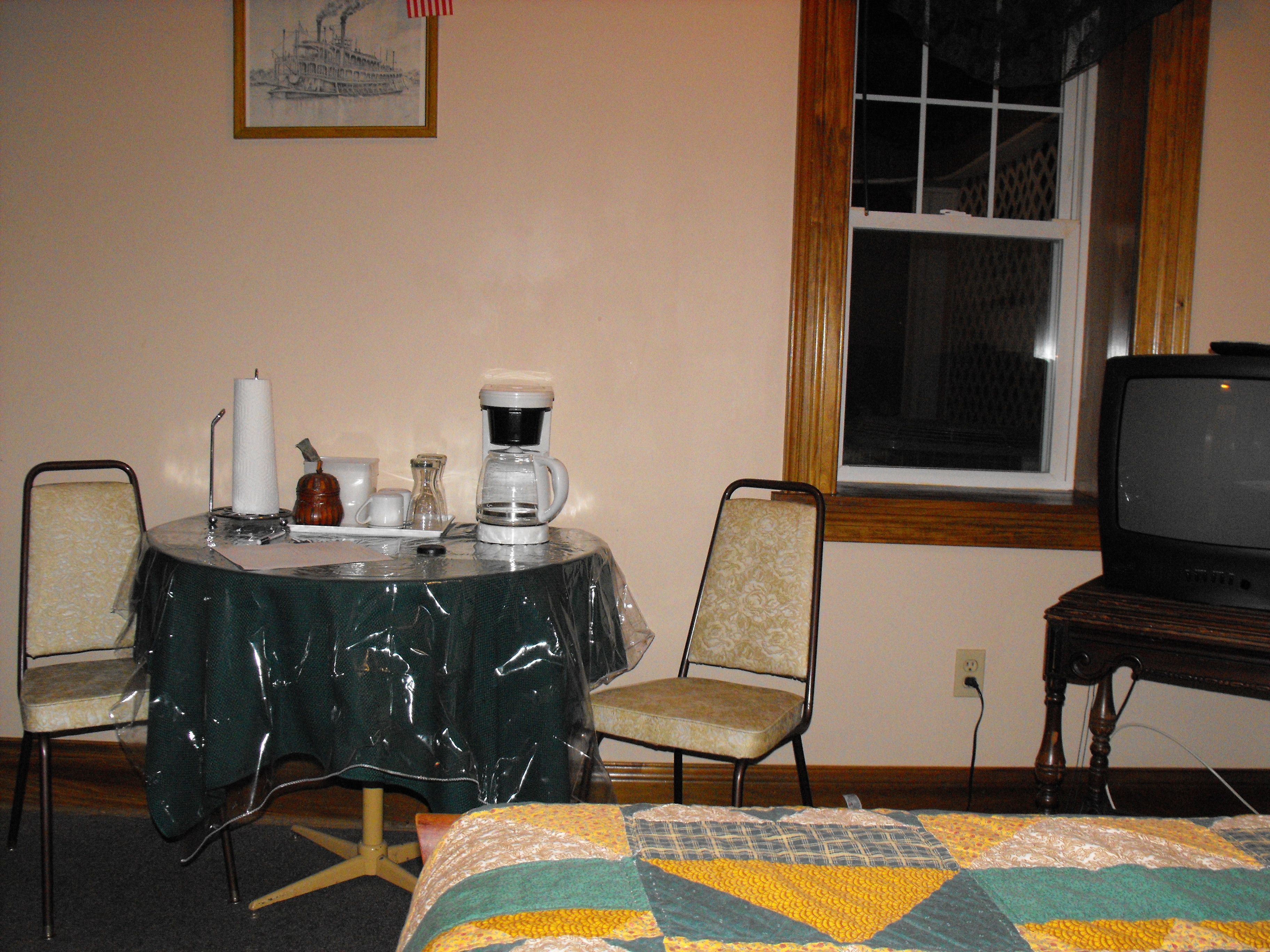 Une chambre d’hôtel avec un lit, une table avec une machine à café, deux chaises, une télévision et une fenêtre donnant sur un paysage agréable.