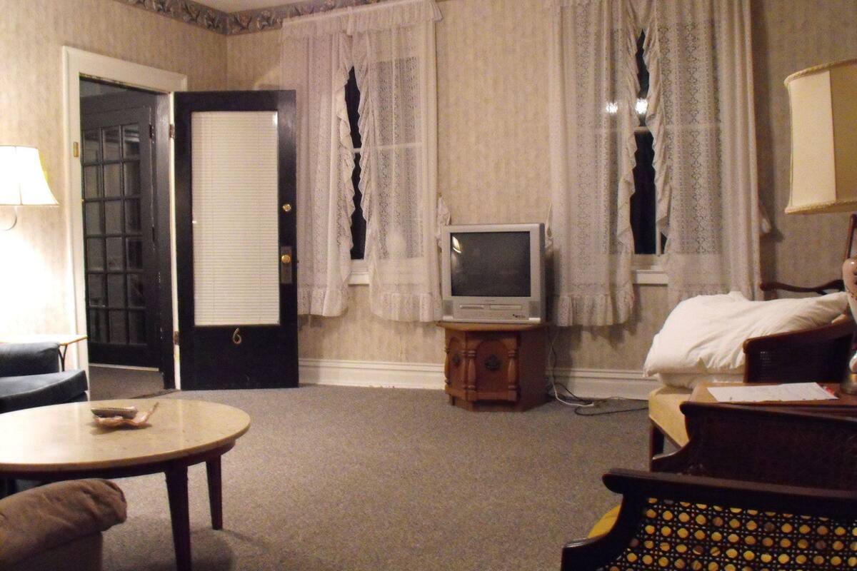 Ein Hotelzimmer mit einem Bett, einem Fernseher auf einem Holzboden, einem kleinen Tisch und einem Sessel.