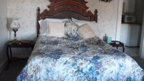 Une chambre à coucher avec un lit en bois, une literie à motifs floraux, une table de chevet avec une lampe et un mur recouvert d’un papier peint à fleurs.