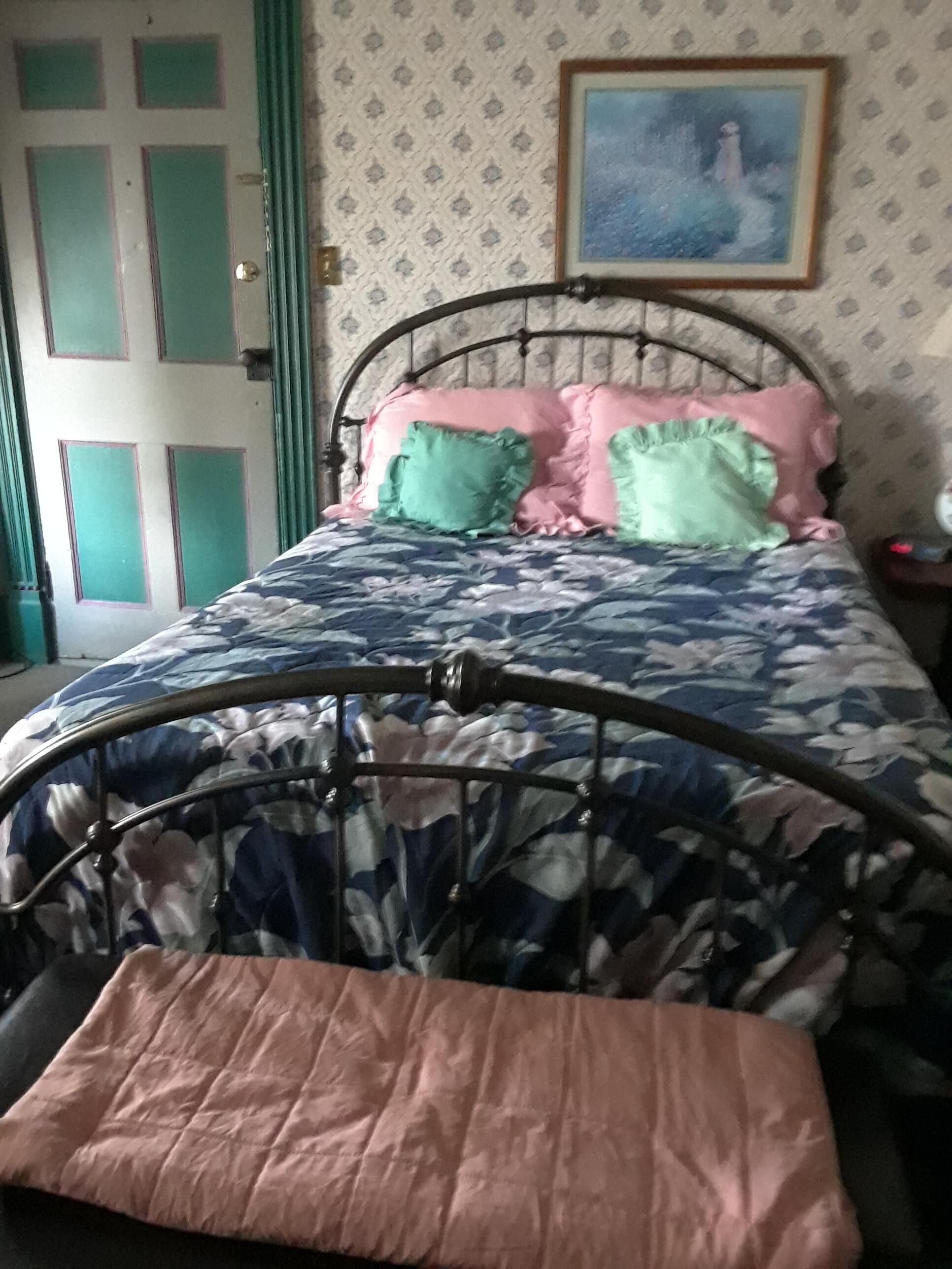 A bed with a metal frame, a floral-patterned bedspread, and a pink pillow.