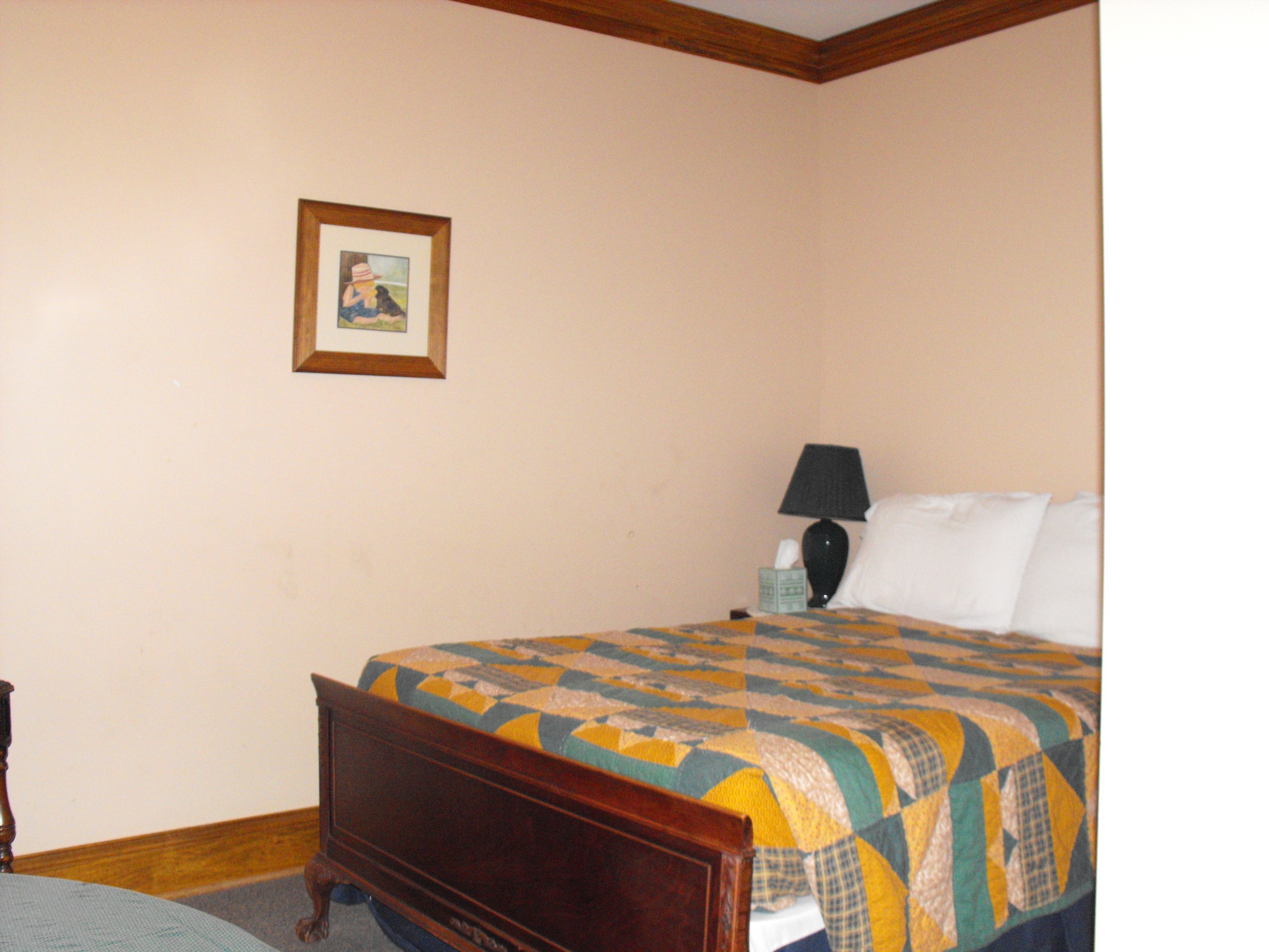 A bedroom with a wooden bed, a quilt, a bedside lamp, a nightstand, and a framed picture on the wall.