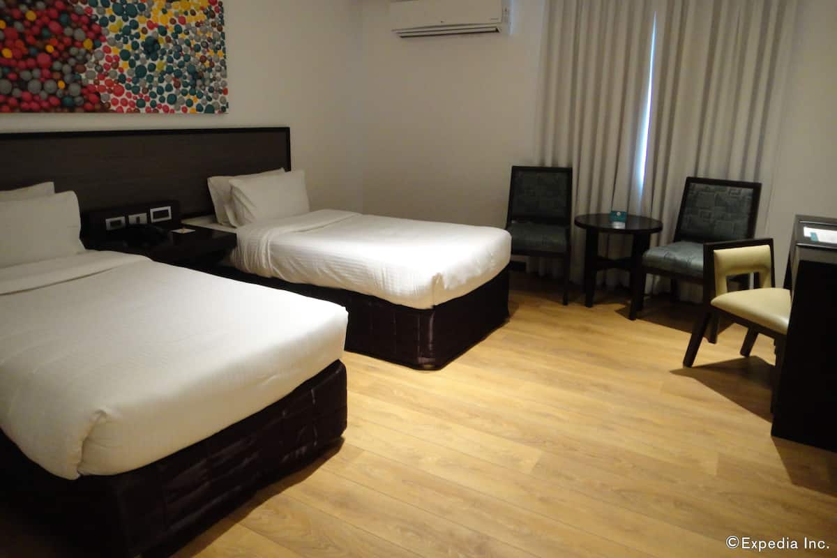 A hotel room with two beds, a desk, a chair, a small table, and a colorful artwork on the wall.