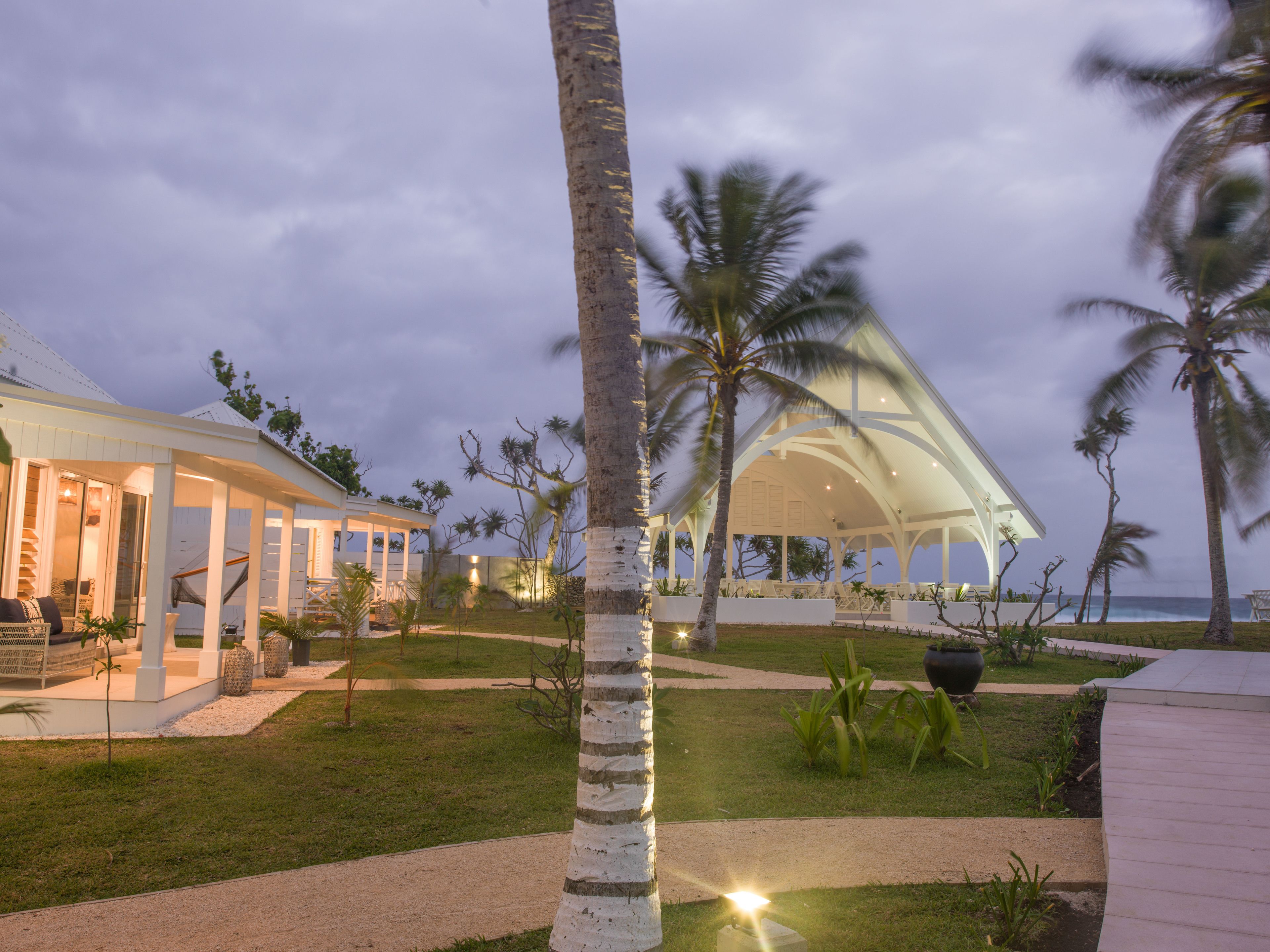 A resort with a covered outdoor area, palm trees, and a view of the ocean.
