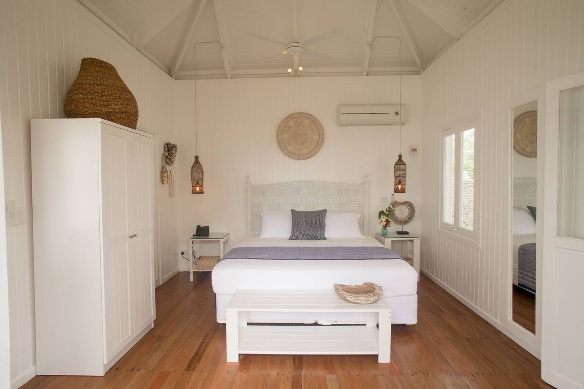 A bedroom with a large bed, a wardrobe, a bedside table, a mirror, and a ceiling fan.