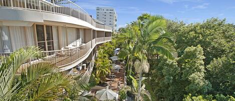 A hotel with a balcony, outdoor seating, and lush greenery.